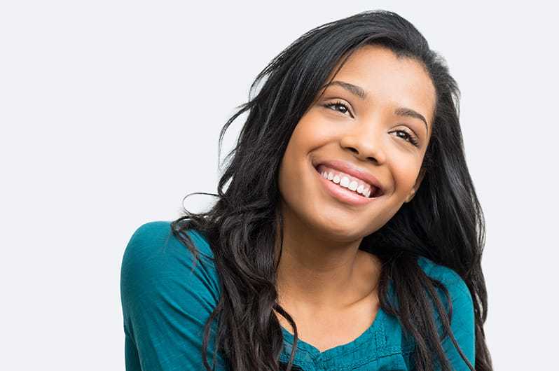 Smiling woman with long hair in a teal shirt looking upwards against a light background.