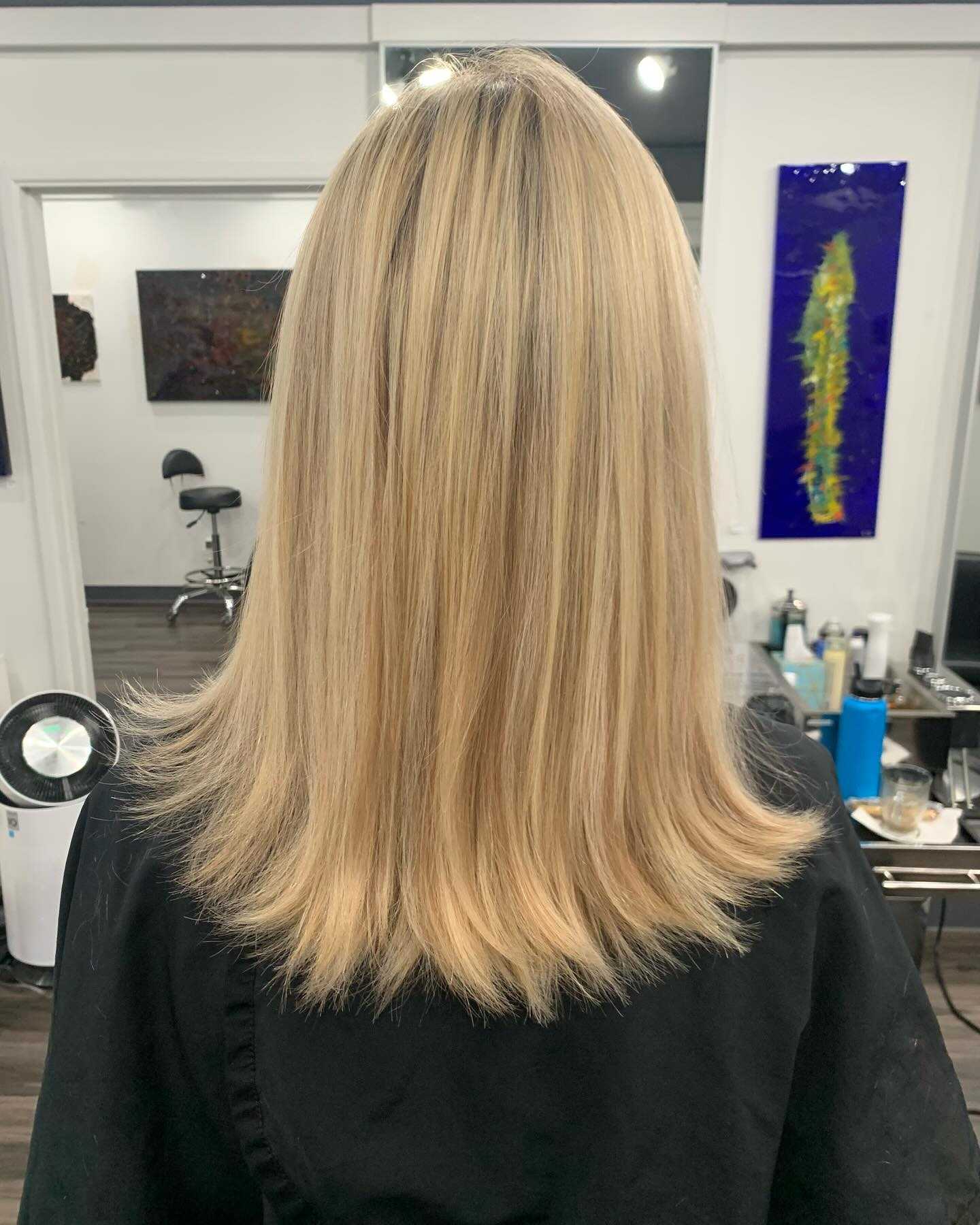 Blonde hair with straight haircut in a salon setting, seen from the back.