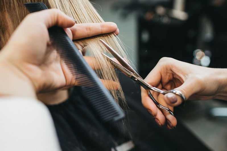 Hairdresser cutting blond hair with scissors and comb.