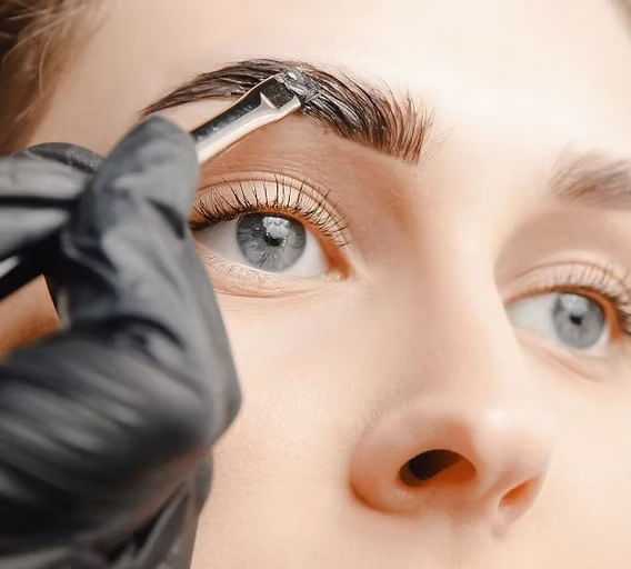 Person's eyebrows being shaped with tweezers wearing black gloves.