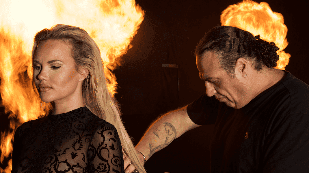 Stylist prepares woman's hair near large flames, creating a dramatic scene.