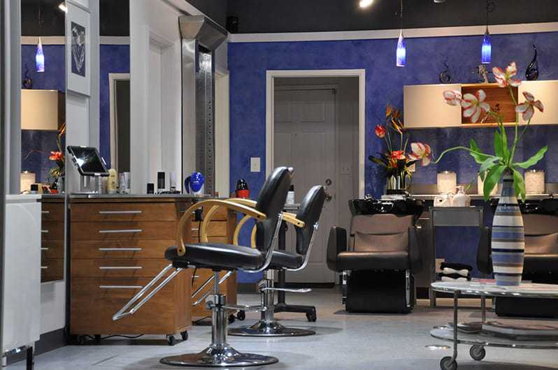 Modern hair salon interior with blue walls, styling chairs, and vibrant floral decor.