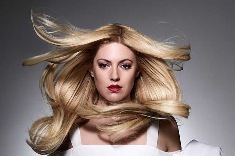 Blonde woman with flowing hair and red lipstick in dramatic lighting.
